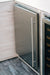 Stono Outdoor Living A close-up of the TrueFlame 24" 5.1 Cu. Ft. Outdoor Rated Refrigerator (Right Hinge) - AMD-RFR-24S-B, featuring a long vertical handle, set flush with light wood cabinetry and a dark wood floor.
