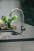 Stono Outdoor Living The TrueFlame TF-NK-19U 19" x 15" stainless steel undermount sink is set in a gray countertop, paired with a modern stainless steel faucet. In the background, a wooden tray displays lemons and green leaves.
