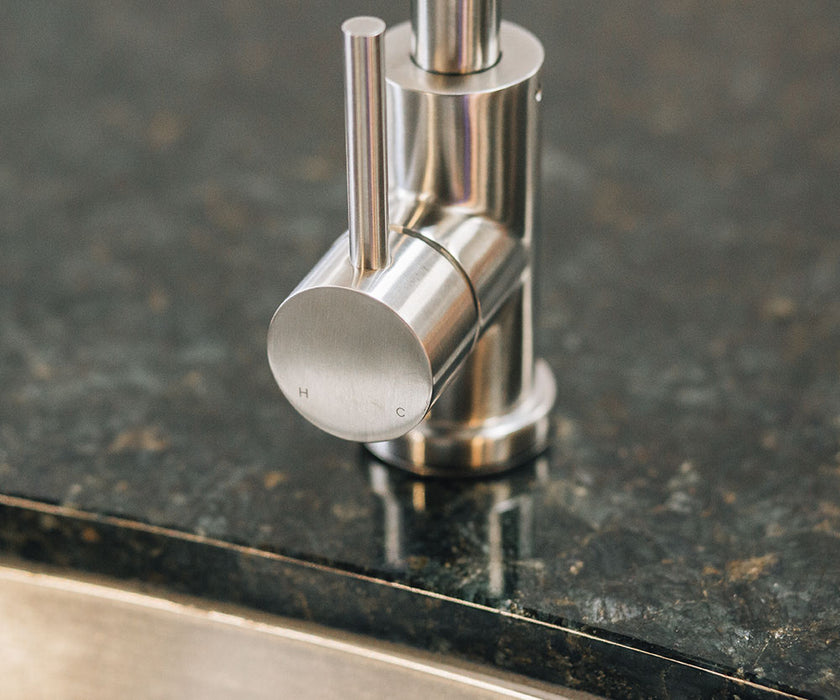 Stono Outdoor Living Close-up of a modern stainless steel faucet handle on a dark granite countertop beside the TrueFlame 19" x 15" Stainless Steel Undermount Sink (TF-NK-19U), with H and C markings for hot and cold water.