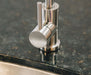 Stono Outdoor Living Close-up of a modern stainless steel faucet handle on a dark granite countertop beside the TrueFlame 19" x 15" Stainless Steel Undermount Sink (TF-NK-19U), with H and C markings for hot and cold water.