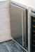 Stono Outdoor Living A close-up of the TrueFlame 24" 5.3 Cu. Ft. Deluxe Outdoor Rated Refrigerator (TF-RFR-24D-R) showcases its modern stainless steel design with a vertical handle, seamlessly integrated into light wood cabinetry beside a glass-door wine cooler.