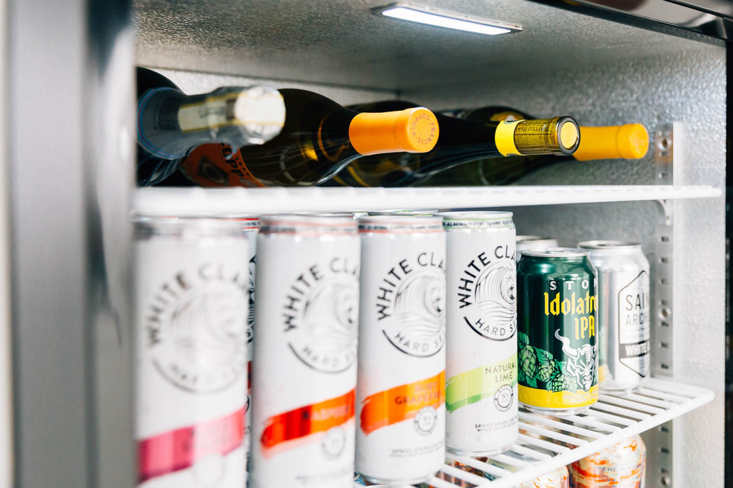 Stono Outdoor Living Cans of White Claw, craft beer, and white wine bottles are neatly arranged inside the TrueFlame 24" Deluxe Outdoor Refrigerator (TF-RFR-24D-R) with a sleek stainless steel door.