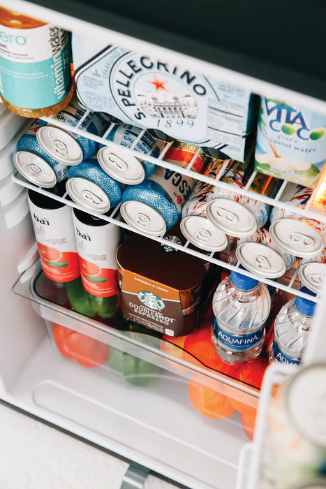 Stono Outdoor Living An open TrueFlame 22" 4.1c Deluxe Outdoor Approved Fridge (AMD-RFR-22D) by TrueFlame is stocked with sparkling water, coconut water, canned drinks, Vitaminwater, Aquafina bottles, cold brew coffee, and produce in the lower drawer.