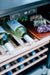 Stono Outdoor Living The TrueFlame 24" 5.3 Cu. Ft. Outdoor Rated Wine Cooler features stainless steel, wooden shelves for white wine, a digital temperature display, and a snack board on top—ideal for any outdoor kitchen setup.