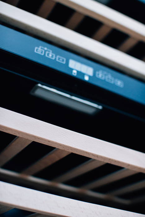 Stono Outdoor Living Close-up of wooden shelves and softly focused horizontal slats inside the TrueFlame 24" 5.3 Cu. Ft. Outdoor Rated Dual Zone Wine Cooler, shown with its digital control panel.