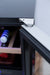 Stono Outdoor Living Close-up of the TrueFlame 15" 3.2 Cu. Ft. Outdoor Rated Single Zone Wine Cooler (AMD-RFR-15W) door hinge in focus, showing wine bottles on a wooden shelf—ideal for outdoor kitchens and refrigeration by TrueFlame.
