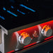 Stono Outdoor Living Close-up of a TrueFlame 32" 4-Burner Built-In Natural Gas Grill (TF32) with two orange-lit control knobs labeled TrueFlame and visible blue flames inside, showing the grill is on and heating.