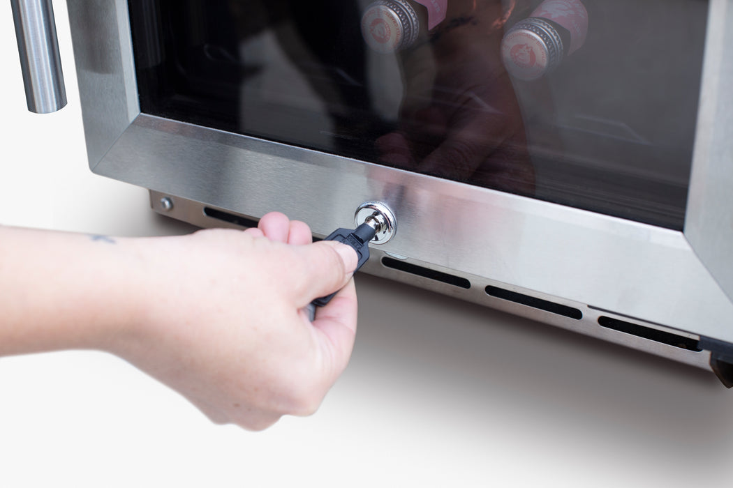 Stono Outdoor Living A hand inserts a key into the lock of the TrueFlame 15" 3.2 Cu. Ft. Outdoor Rated Single Zone Wine Cooler, with bottles visible inside through its glass door.