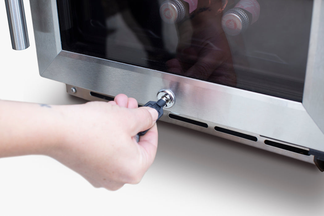Stono Outdoor Living A hand inserts a key into the lock of the TrueFlame 15" Outdoor Rated Dual Zone Wine Cooler (AMD-RFR-15WD), a sleek stainless steel appliance with a glass door showing bottles inside.