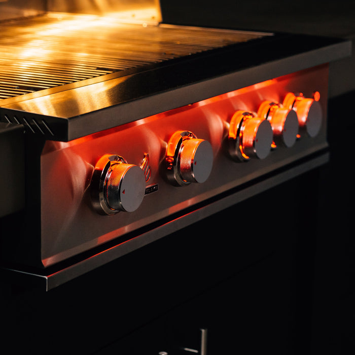 Stono Outdoor Living Close-up of the TrueFlame 32" 4-Burner Built-In Natural Gas Grill (TF32), featuring four large control knobs with glowing orange lights reflecting on the stainless steel and metal grates above, highlighted in dim lighting.