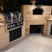 Stono Outdoor Living A modern outdoor kitchen showcases the Wildfire Ranch Pro 42" Black Stainless Steel Gas Grill by Wildfire Outdoor Living with four knobs, next to a built-in stone pizza oven on a stone countertop atop a tiled patio at night.