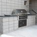 Stono Outdoor Living The Wildfire Ranch Pro 36" Gas Grill 304 Black SS by Wildfire Outdoor Living is built into a modern outdoor kitchen with gray concrete block walls, a black countertop, and two stone platters on display.
