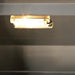 Stono Outdoor Living A close-up of a rectangular under-cabinet light fixture emitting a warm glow, mounted beneath a dark shelf in an outdoor kitchen near the Delta Heat 38-Inch 3-Burner Built-In Propane Gas Grill (DHBQ38G-DL) by Delta Heat.