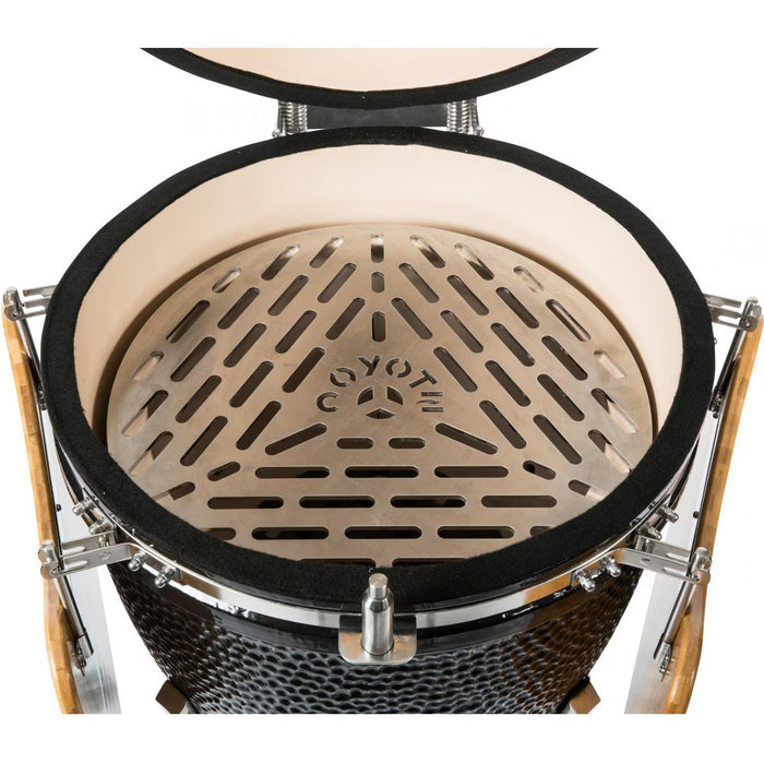 Stono Outdoor Living Top view of a Coyote Asado Smoker w/ Stand & Side Shelves (C1CHCS-FS), featuring a kamado-style charcoal grill with the COYOTE-branded grate, textured black ceramic exterior, and metal hinges—perfect for outdoor cooking.