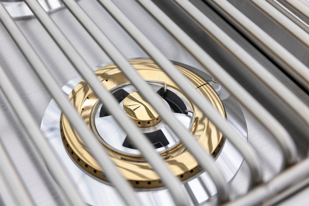 Stono Outdoor Living Close-up of the Blaze Premium LTE+ Natural Gas Stainless Steel Double Side Burner w/ Lid (BLZ-SB2-LTE3-NG) by Blaze, featuring sleek brass and silver components under parallel grates—ideal for a clean, modern outdoor kitchen.
