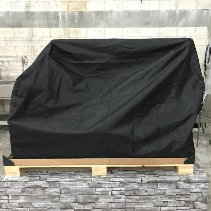 Stono Outdoor Living A large object covered with the Tagwood BBQ Grill Cover for BBQ25SS Grill (BBQ87SS) by Tagwood BBQ sits on a wooden pallet on a stone-patterned surface, with a concrete block wall in the background.
