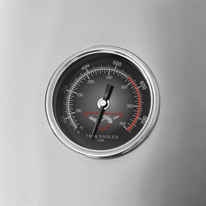 Stono Outdoor Living A close-up shows the Twin Eagles 36-Inch 3-Burner Built-In Natural Gas Grill (TEBQ36G-CN) with a round stainless steel thermometer, displaying temperatures from 100°F to 700°F in Fahrenheit and Celsius. The Twin Eagles brand is visible on the dial.