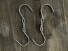 Stono Outdoor Living Two Tagwood BBQ Extended S-Shape Meat Hooks (BBQ75SS), made of shiny 304 stainless steel, sit parallel on a rustic wooden surface. Their sharp points are perfect for meat smoking or other hanging tasks. Brand: Tagwood BBQ.