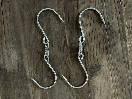Stono Outdoor Living Two Tagwood BBQ Extended S-Shape Meat Hooks (BBQ75SS), made of shiny 304 stainless steel, sit parallel on a rustic wooden surface. Their sharp points are perfect for meat smoking or other hanging tasks. Brand: Tagwood BBQ.