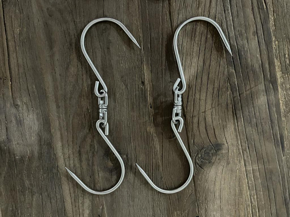 Stono Outdoor Living Two Tagwood BBQ Extended S-Shape Meat Hooks (BBQ75SS), made of shiny 304 stainless steel, sit parallel on a rustic wooden surface. Their sharp points are perfect for meat smoking or other hanging tasks. Brand: Tagwood BBQ.