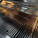 Stono Outdoor Living Close-up of a clean, empty TrueFlame 32" 4-Burner Built-In Natural Gas Grill (TF32) with metal grates, displaying reflections of light on the shiny stainless steel commercial-grade surface.