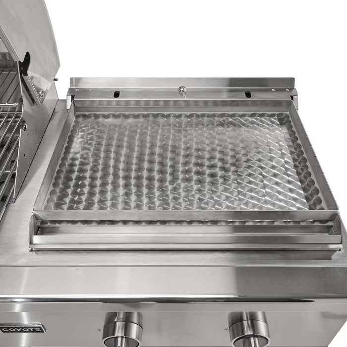 Stono Outdoor Living Close-up of the Coyote 50" Combo Grill (C3CO50NG), showing a stainless steel griddle for flat-top cooking, two front control knobs, and a partially open hood with a small warming rack on the left.