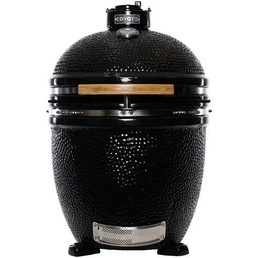 Stono Outdoor Living The Coyote Asado Smoker, Built-In (C1CHCS), is a black ceramic kamado-style charcoal grill with a domed lid, wooden handle, temperature gauge, and air vents on sturdy legs—ideal for outdoor cooking.