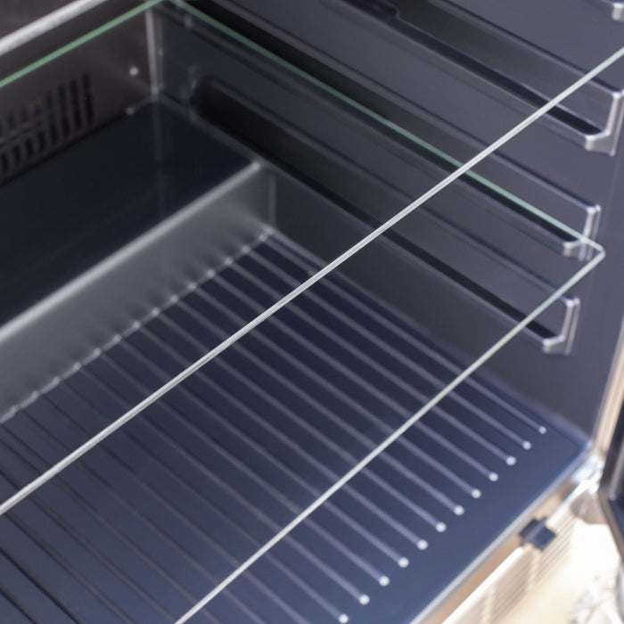 Stono Outdoor Living Close-up of the TrueFlame 24" 5.1 Cu. Ft. Outdoor Rated Refrigerator (AMD-RFR-24G) showcasing its clear glass shelves and clean, dark interior behind the glass door.