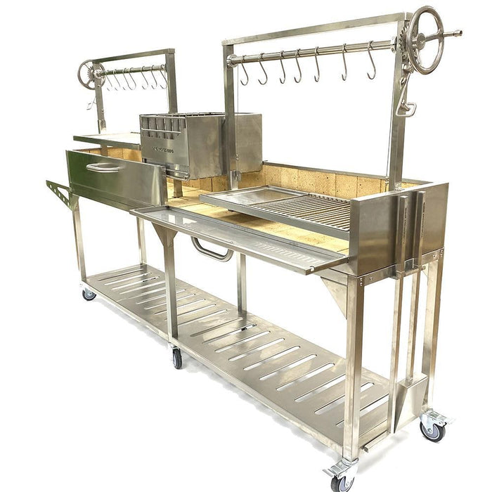 Stono Outdoor Living The Tagwood BBQ Double Argentine Santa Maria Wood Fire & Charcoal Grill (BBQ04SS) offers a modern stainless steel design on wheels, utensil hooks, open fire grill surface, rotisserie attachment, side tray, and lower storage shelf.