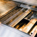 Stono Outdoor Living Close-up of the TrueFlame 40" 5-Burner Built-In Natural Gas Grill - TF40, featuring commercial-grade stainless steel grates and a perforated tray, with sleek, modern surfaces reflecting warm light.