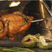 Stono Outdoor Living A whole chicken on the rotisserie inside the Twin Eagles Wi-Fi Controlled 36-Inch Pellet Grill and Smoker (TEPG36R), garnished with rosemary, with artichokes and asparagus grilling nearby—a top choice for premium outdoor cooking.