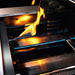 Stono Outdoor Living Close-up of the TrueFlame 40" 5-Burner Built-In Propane Gas Grill (TF40L) with blue and orange-yellow flames reflecting off its high-performance stainless steel surfaces.