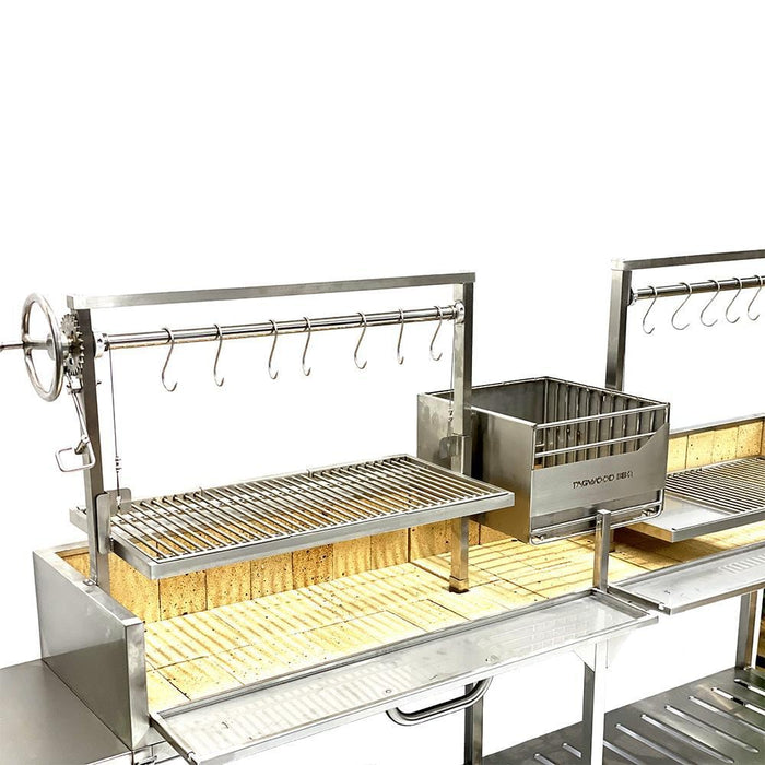 Stono Outdoor Living The Tagwood BBQ Double Argentine Santa Maria Wood Fire & Charcoal Grill (BBQ04SS) by Tagwood BBQ features a stainless steel build with a wheel crank, metal hooks, rectangular grate, and firebox—ideal for open fire grilling on a brick-lined base.
