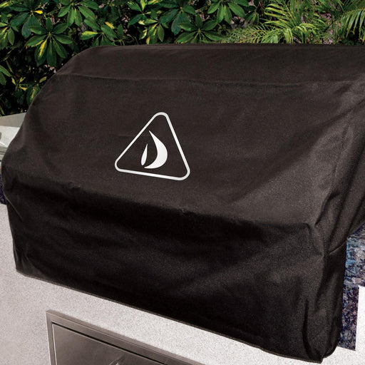 Stono Outdoor Living The Delta Heat Grill Cover for 38-Inch Built-In Grill (VCBQ38-C) in black vinyl, featuring a white sailboat logo inside a triangle, protects a built-in gas grill. Green leafy plants are visible in the background.