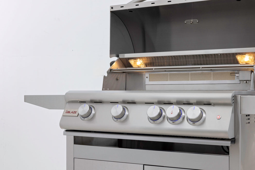 Stono Outdoor Living The Blaze Premium LTE+ Marine Grade 32" 4-Burner Propane Grill (BLZ-4LTE3MG-LP) features four control knobs, a side shelf, internal grill lights, and a stainless steel lid open to reveal a spacious cooking surface with rear infrared burner.