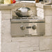Stono Outdoor Living A Coyote Wok for Power Burner (CWOK) by Coyote sits atop a stainless steel outdoor gas stove with two knobs, built into a stone counter. A covered pot, fresh vegetables, and a cutting board suggest an upcoming stir-fry.