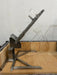 Stono Outdoor Living The Tagwood BBQ Basement Grill - BBQ94SS by Tagwood BBQ features an SS 304 clamp grill rack with angled slots, mounted on a sturdy frame and set on light-colored bricks in a basement against a plain white wall. The rack is designed to hold items at an angle.