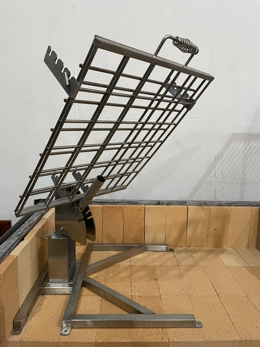 Stono Outdoor Living The Tagwood BBQ Basement Grill - BBQ94SS features an SS 304 metal grill cage with a handle and tilting mechanism, mounted on a stand over beige firebrick-lined base—ideal for grilling or cooking in your basement setup.
