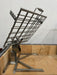 Stono Outdoor Living The Tagwood BBQ Basement Grill - BBQ94SS features an SS 304 metal grill cage with a handle and tilting mechanism, mounted on a stand over beige firebrick-lined base—ideal for grilling or cooking in your basement setup.