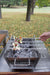 Stono Outdoor Living Someone grills vegetable and meat skewers outdoors in a park using the Tagwood BBQ Set of 2 Stainless Steel Skewers (BBQ89) on a portable charcoal grill, with trees and fallen leaves in the background.