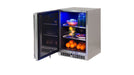 Stono Outdoor Living The Lynx 24" Outdoor Refrigerator (LN24REF) by Lynx is shown with its door open, illuminated by a blue interior light and shelves stocked with bottles, fruit bowls, lemons, apples, and oranges.