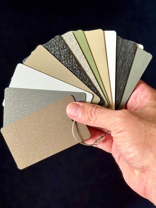 Stono Outdoor Living A hand displays Stono Outdoor Living's Color and Material Sample Kit—fanned powder-coated aluminum samples in neutral tones like beige, gray, green, and black—ideal for premium outdoor kitchen finishes against a dark background.