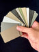 Stono Outdoor Living A hand displays Stono Outdoor Living's Color and Material Sample Kit—fanned powder-coated aluminum samples in neutral tones like beige, gray, green, and black—ideal for premium outdoor kitchen finishes against a dark background.