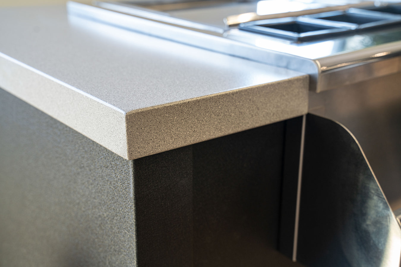 Stono Outdoor Living Close-up of a kitchen countertop with a smooth, light gray surface next to a stainless steel appliance, highlighting the clean lines and modern design.