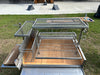 Stono Outdoor Living The Tagwood BBQ Round Warming Roof Grill for BBQ23SS/BBQ25SS - BBQ99SS by Tagwood BBQ is a large 304 stainless steel outdoor grill with multiple racks, a warming rack, and spacious cooking area, shown on grass beside folding chairs and a side table.