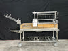 Stono Outdoor Living The Tagwood BBQ Argentine Santa Maria Wood Fire & Charcoal Grill (BBQ26SS) features 304 stainless steel, wood accents, wheels, grilling racks, hooks, a side basket, and a handle—classic Argentine design—shown on a plain black background.