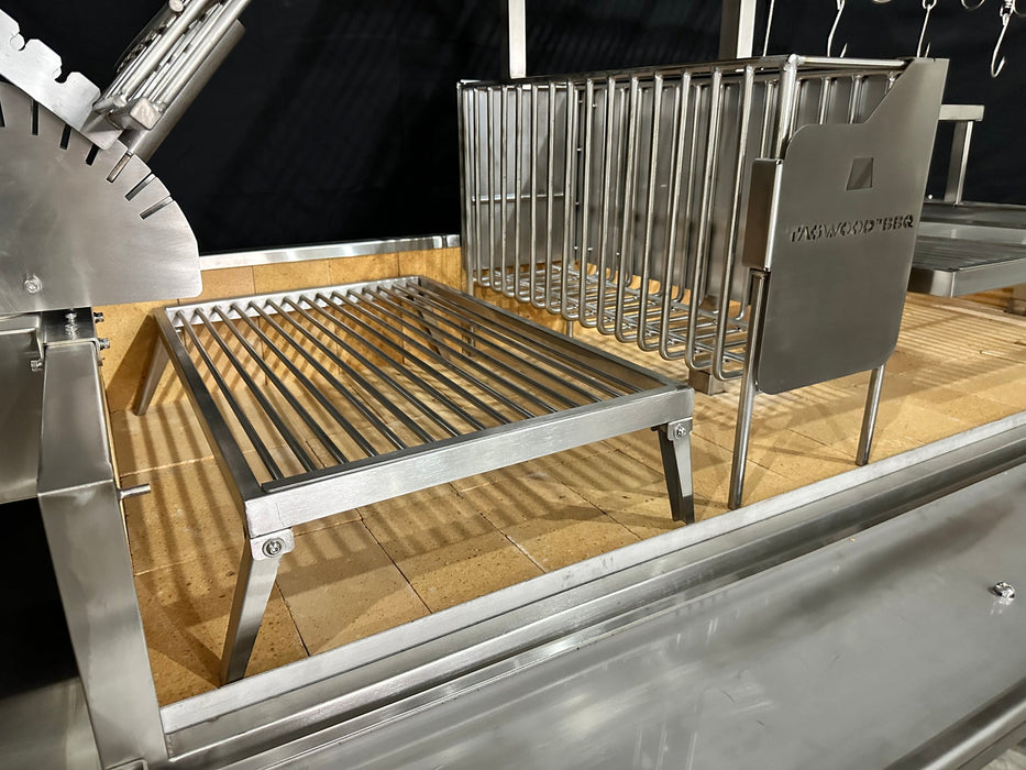 Stono Outdoor Living A close-up of the Tagwood BBQ Argentine Santa Maria Wood Fire & Charcoal Grill – BBQ26SS, made from 304 stainless steel with a removable grilling rack and vertical meat racks, placed on a tiled base against a dark background.