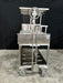 Stono Outdoor Living The Tagwood BBQ Argentine Santa Maria Wood Fire & Charcoal Grill - BBQ26SS, featuring a 304 stainless steel cart with wheels, metal shelves, and a hand crank, is set against a black backdrop on a concrete floor.