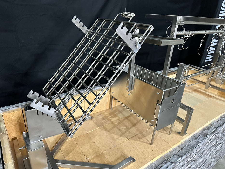 Stono Outdoor Living The Tagwood BBQ Basement Grill - BBQ94SS by Tagwood BBQ is displayed on a tiled platform, featuring a large SS 304 grilling rack, rotisserie setup, adjustable grids, metal hooks, and clamp grill in a dark basement setting.