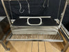 Stono Outdoor Living The Tagwood BBQ Large Top Lid - BBQ59SS by Tagwood BBQ features a stainless steel smoker or roasting box with a spacious lid and handle, placed on a slatted metal rack with hanging hooks above, all set against a black backdrop.